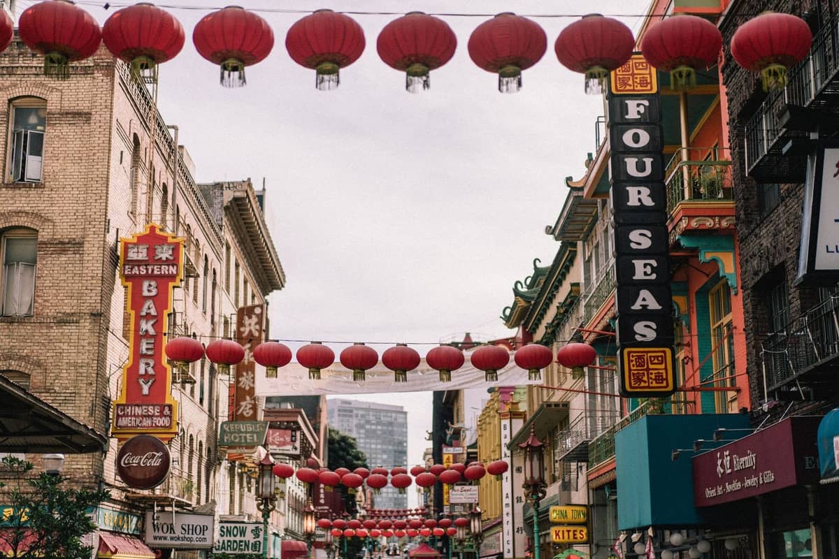 Straßenszene in Chinatown mit hängenden roten Laternen, Geschäften und Restaurantschildern, die eine lebhafte Atmosphäre zum Essen und Einkaufen zeigt.