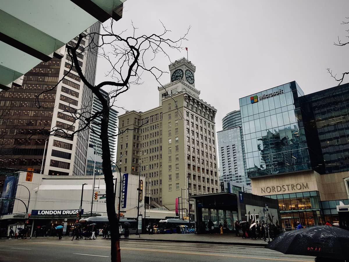 Die Innenstadt von Vancouver an einem regnerischen, bewölkten Tag mit Menschen, die Regenschirme halten, Stadtgebäuden und nassen Straßen.