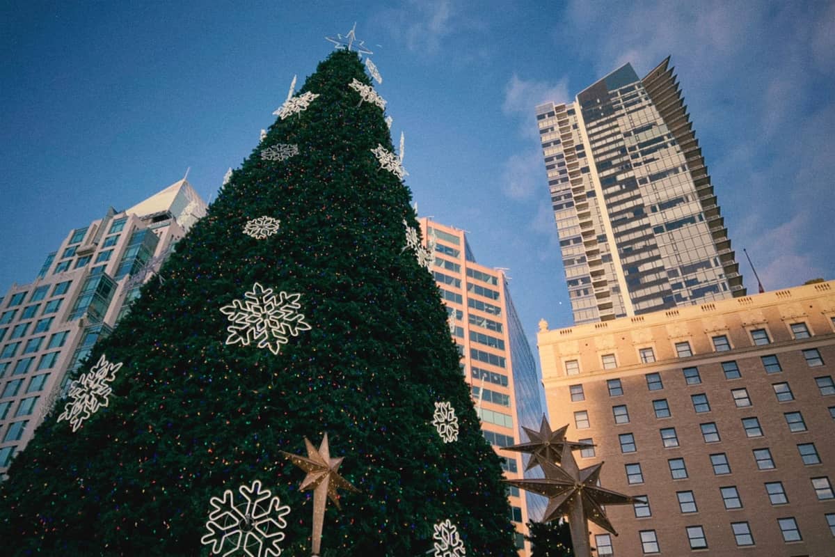 Großer Weihnachtsbaum im Freien, mit Schneeflocken geschmückt, umgeben von Hochhäusern der Innenstadt von Vancouver unter blauem Himmel.