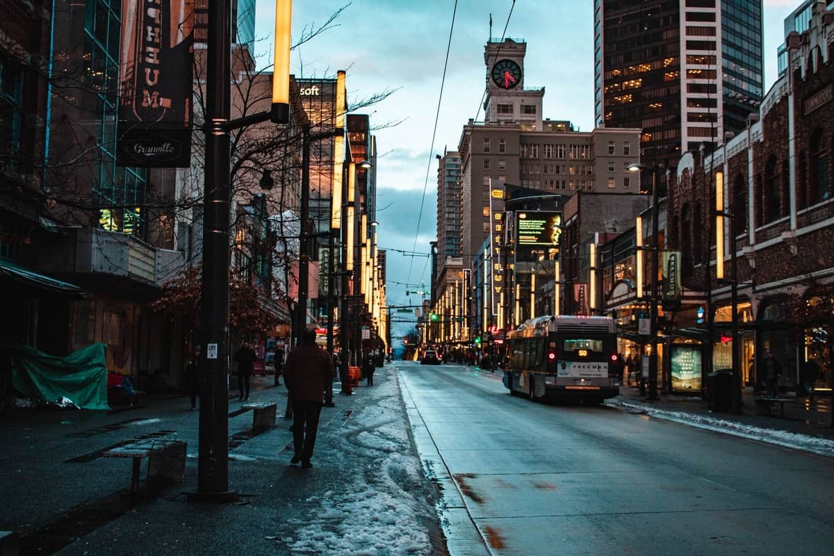 Die Granville Street in der Innenstadt von Vancouver in der Abenddämmerung mit Neonlichtern, Menschen und einem Bus, die die Atmosphäre des Unterhaltungsviertels der Stadt zeigen.