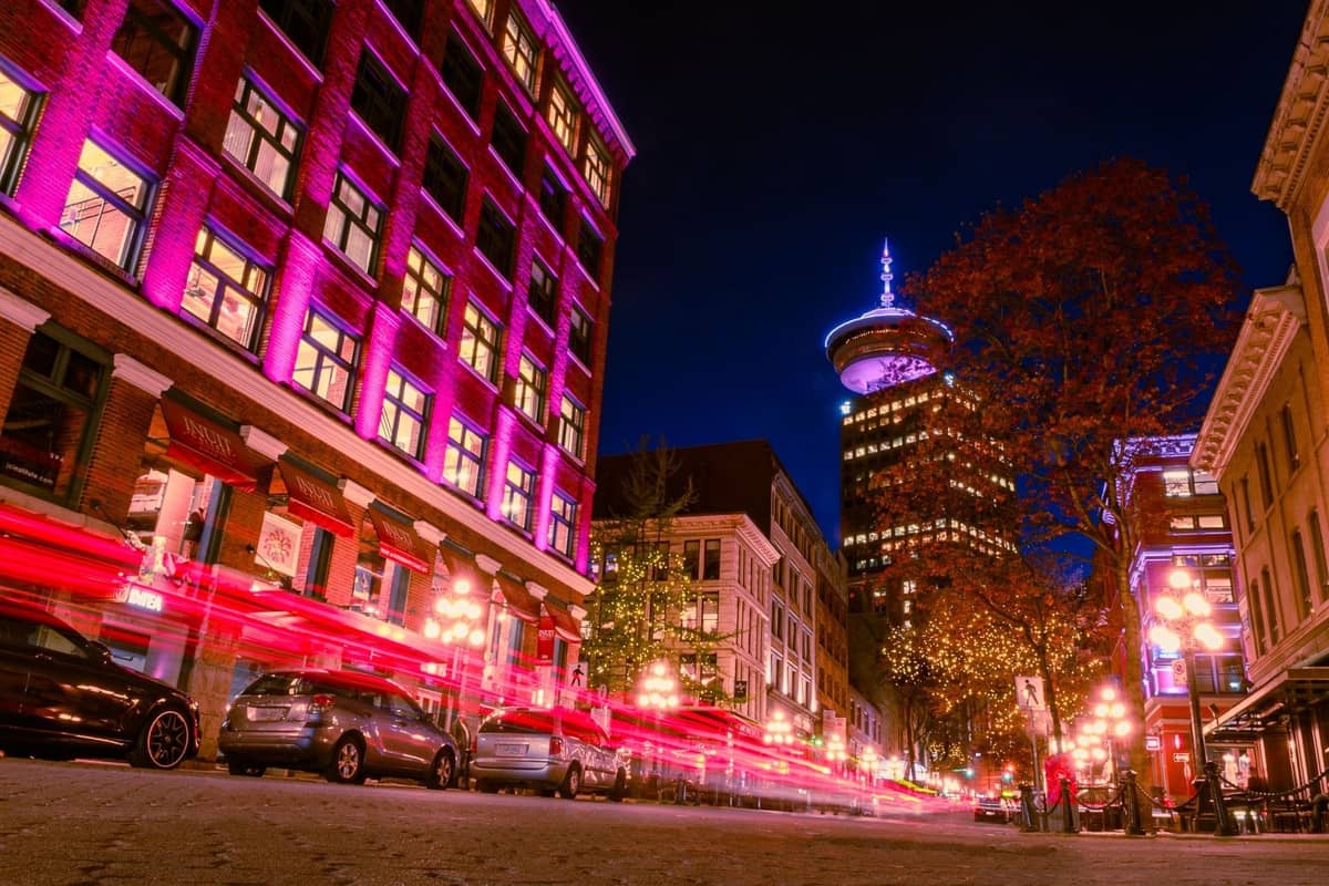Nächtliche Szene in Gastown, Vancouver, mit historischen Gebäuden, lebhaften Lichtern und dem markanten Vancouver Lookout-Turm im Hintergrund.