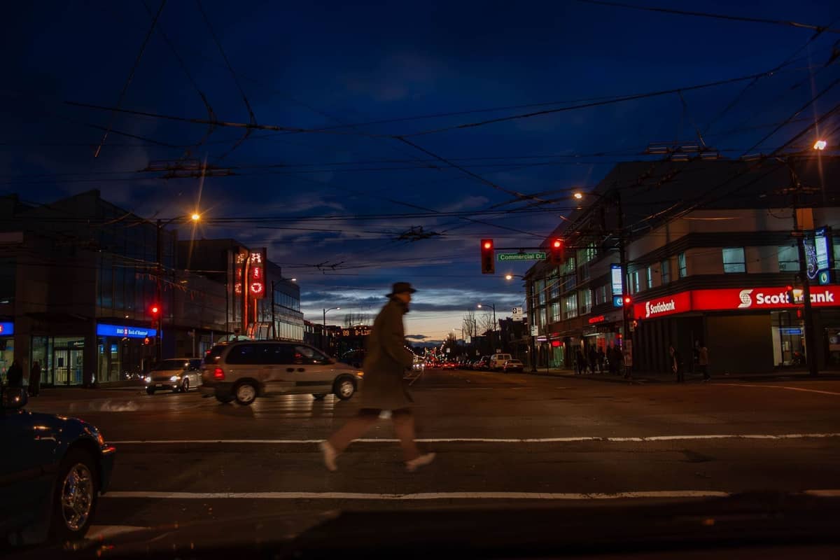 Nächtliche Straßenszene in Vancouver mit Neonlichtern und Menschen, die den Bereich Davie Village überqueren, und lebhaftem Nachtleben.