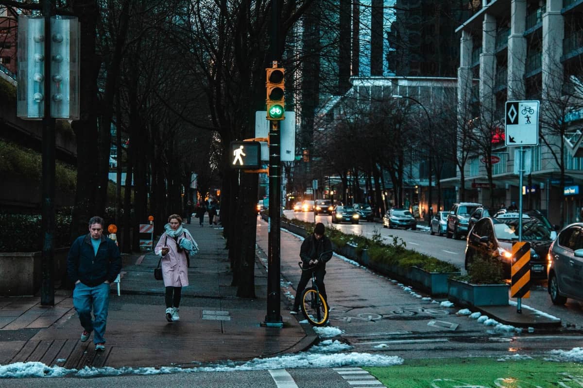 ผู้คนเดินบนถนนที่เปียกในเมือง Vancouver ช่วงฤดูหนาว มีหิมะเล็กน้อยและทางเท้าที่เปียกชื้น พร้อมการจราจรในพื้นหลัง