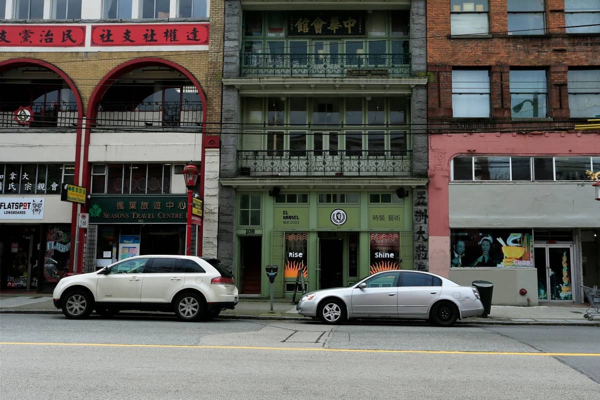 วิวระดับถนนของร้านค้าและอพาร์ตเมนต์เก่าในย่าน Downtown Eastside ของแวนคูเวอร์ พร้อมรถจอดและอาคารที่เก่าทรุดโทรม
