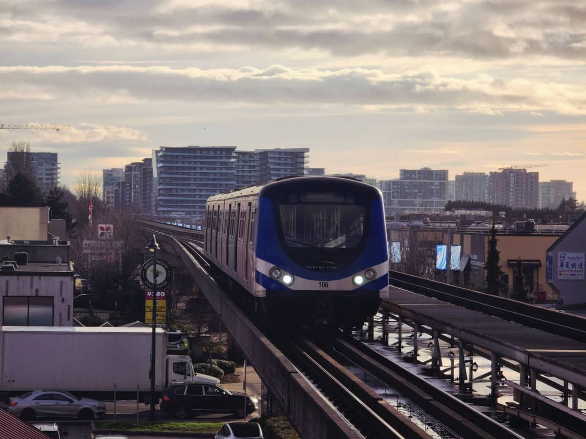 Canada Line SkyTrain-Zug auf erhöhten Gleisen durch Richmond mit Stadtgebäuden im Hintergrund unter bewölktem Himmel.
