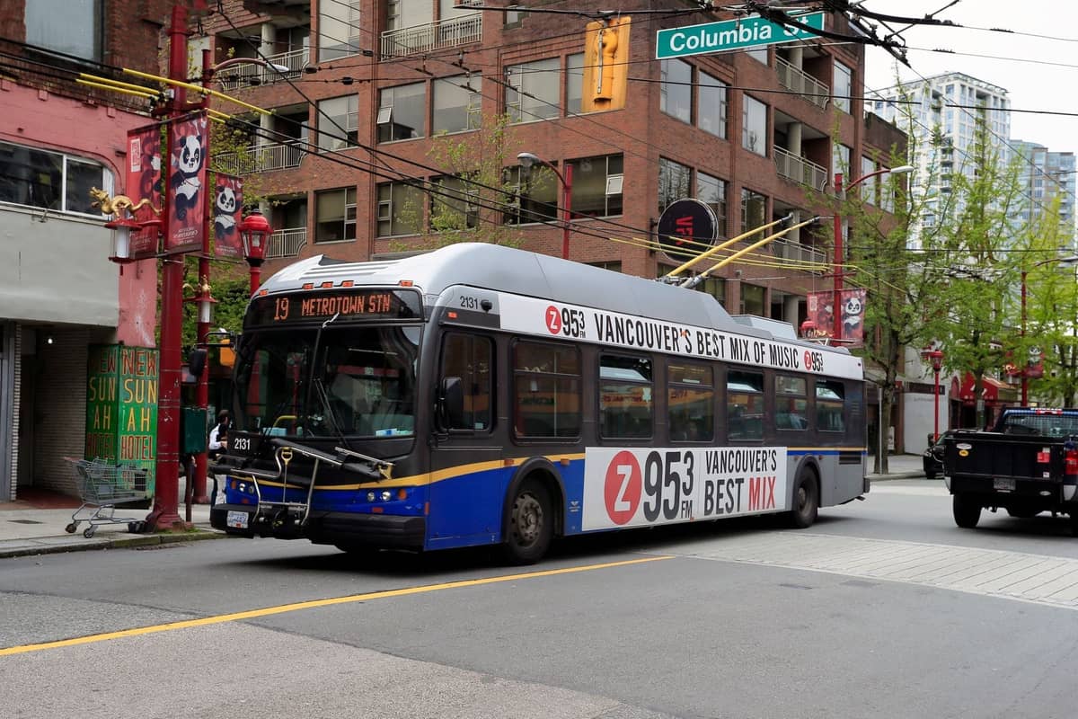 รถบัสประจำเมือง Vancouver วิ่งผ่าน Chinatown โดยมีป้ายแบนเนอร์ริมถนนและอาคารต่างๆ ปรากฏให้เห็นในพื้นหลัง