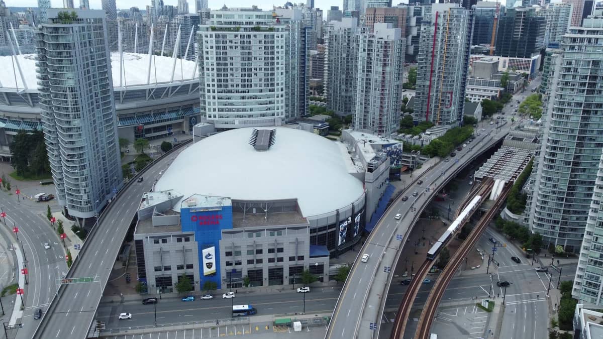Luftaufnahme der Innenstadt von Vancouver mit SkyTrain-Gleisen, einem Zug, der Rogers Arena und dem BC Place Stadion, umgeben von Hochhäusern.
