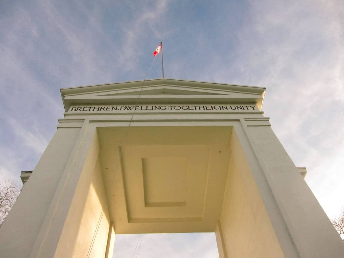 Blick von unten auf das Peace Arch-Monument an der Grenze zwischen Kanada und den USA, mit einer kanadischen Flagge oben und blauem Himmel darüber.