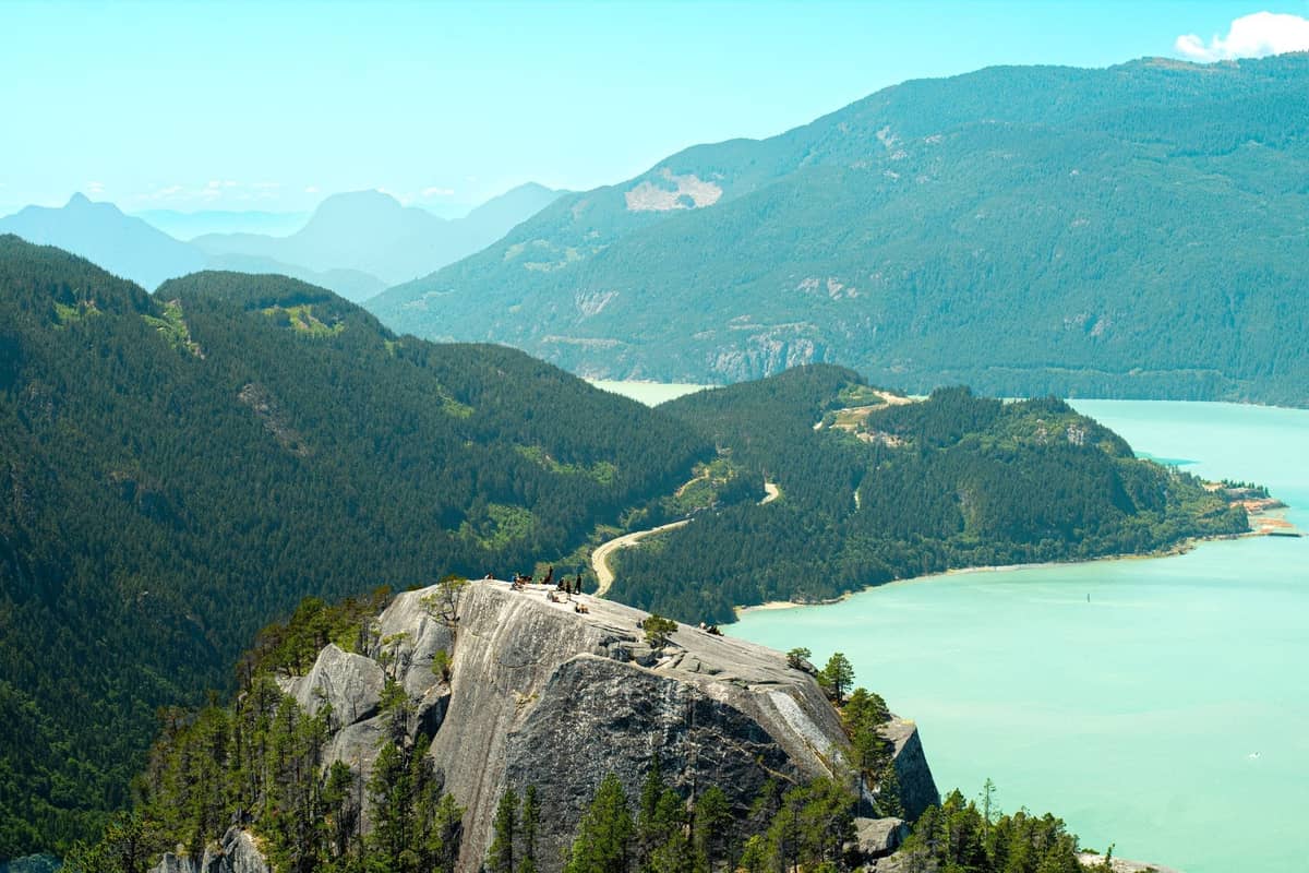Weiter Blick über den Howe Sound mit kurvenreicher Highway, grünen Bergen und Felsvorsprung – klassische Landschaft des Sea to Sky Corridor an einem hellen Tag.