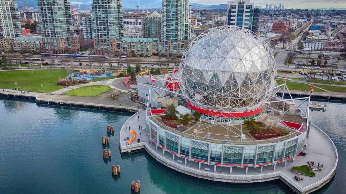 Eine helle Luftaufnahme der geodätischen Kuppel des Science World neben den Uferparks und der Skyline der Innenstadt von Vancouver, die eine der beliebtesten Familienattraktionen der Stadt zeigt.