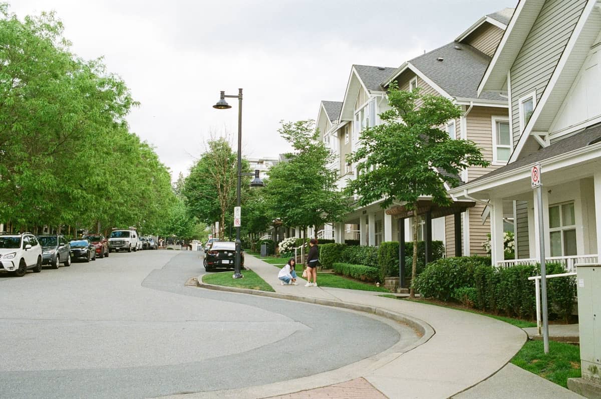 Ruhiges Wohnviertel in Vancouver mit Reihenhäusern, üppigen grünen Bäumen, geparkten Autos und einer Familie, die auf dem Gehweg spaziert.