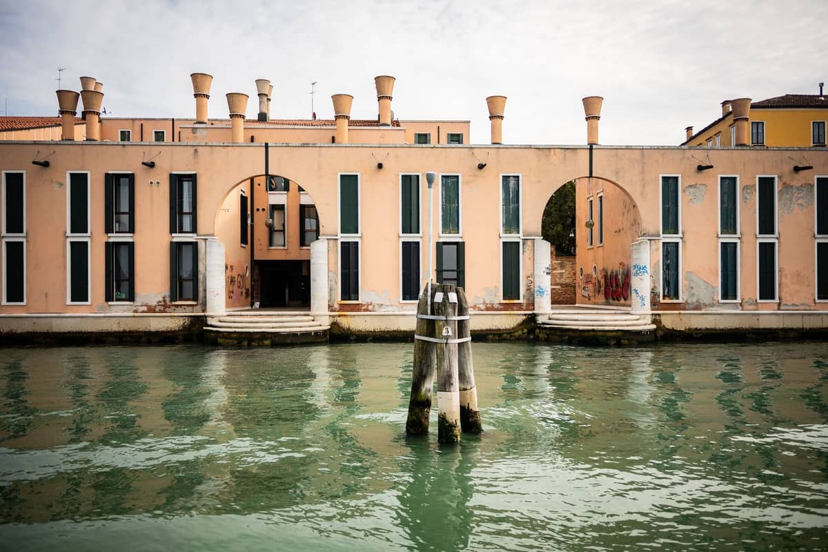 Modernes Ufergebäude mit hohen Säulen und großen Bögen am Arsenale di Venezia, das sich im Wasser spiegelt.