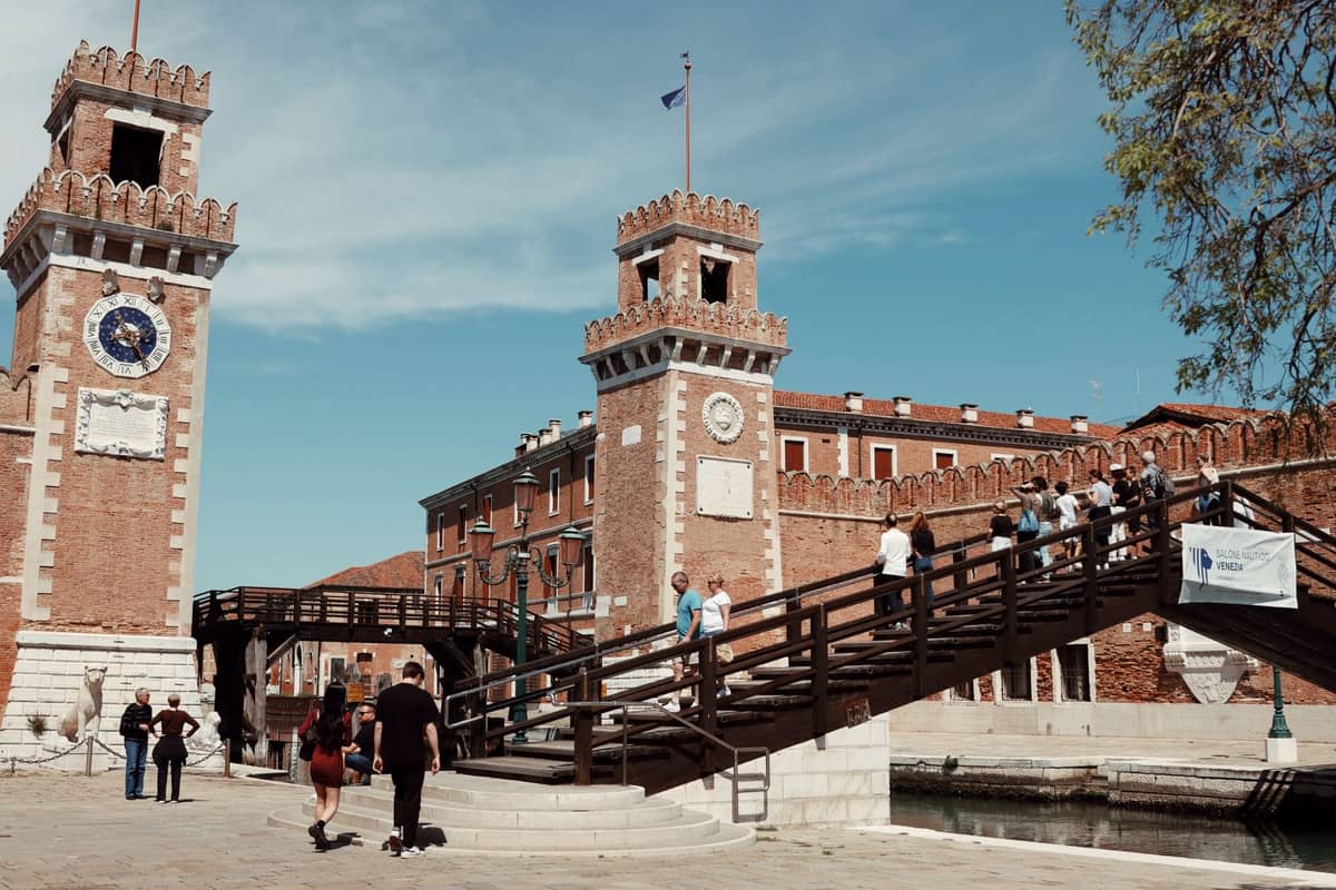 Blick auf das Arsenale in Venedig mit Zwillingstürmen und Menschen, die an einem sonnigen Tag eine hölzerne Fußgängerbrücke überqueren