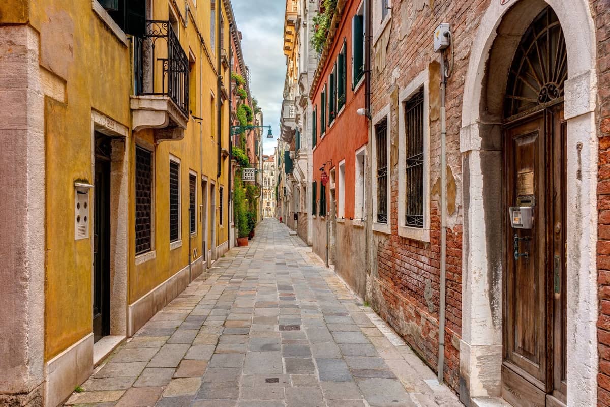 Eine ruhige, schmale Gasse mit bunten Gebäuden auf jeder Seite in Venedig, die eine abgelegene Straße ohne Menschenmassen zeigt.