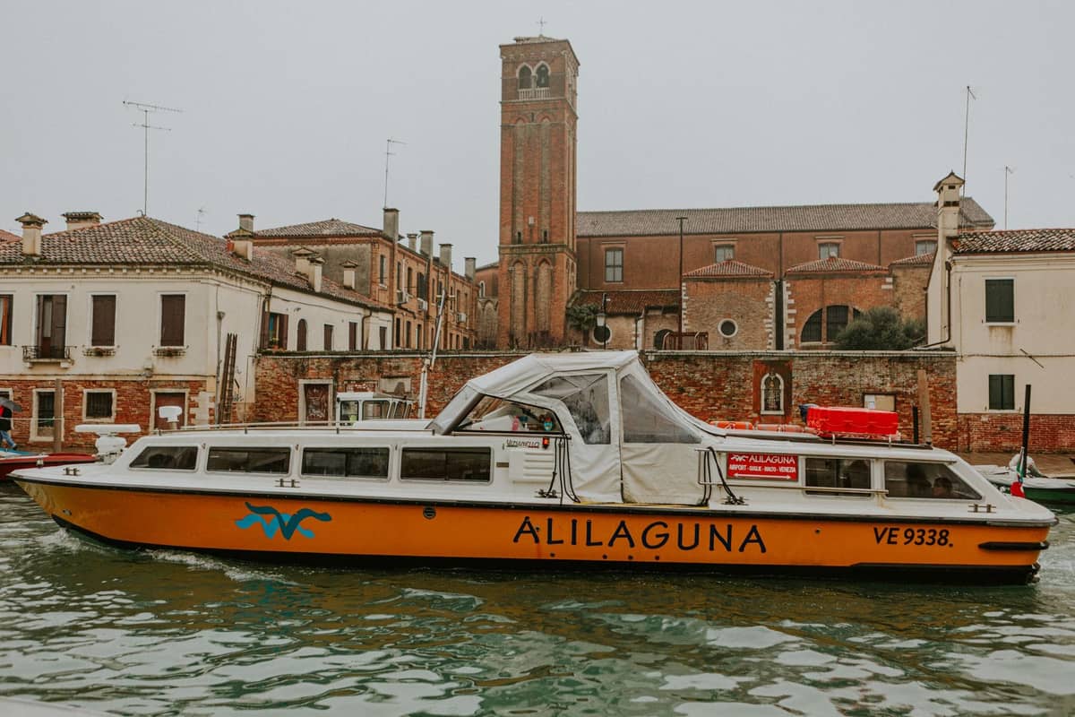 Alilaguna Flughafenboot auf einem Kanal in Venedig, vorbei an historischen Backsteingebäuden und einem hohen Glockenturm an einem grauen Wintertag.