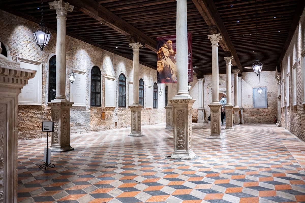 Innenraum eines venezianischen Museums oder historischen Saals mit Säulen, gewölbter Holzdecke, kariertem Boden und klassischem Dekor, gut beleuchtet und ohne Menschenmassen.