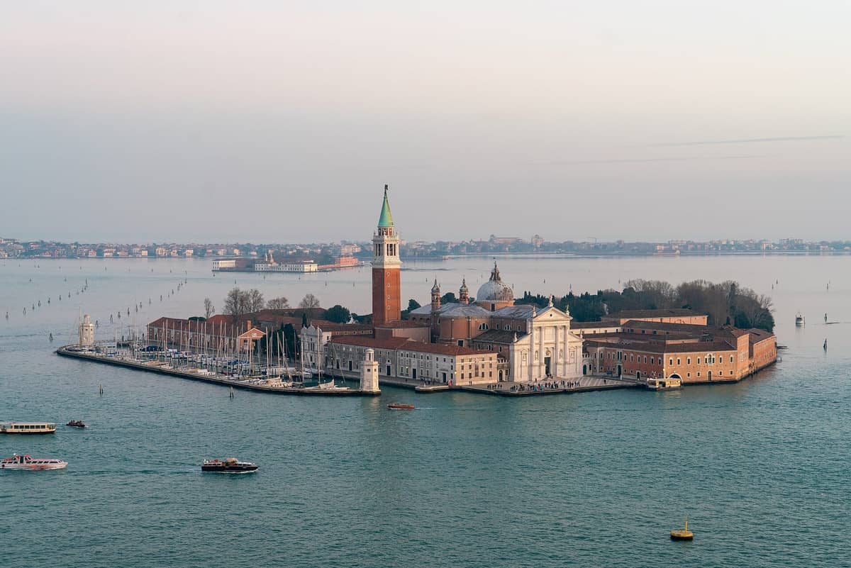 Luftaufnahme der Insel San Giorgio Maggiore mit ihrer Kirche, ihrem Glockenturm und dem Jachthafen, umgeben von Wasser und Booten in Venedig.