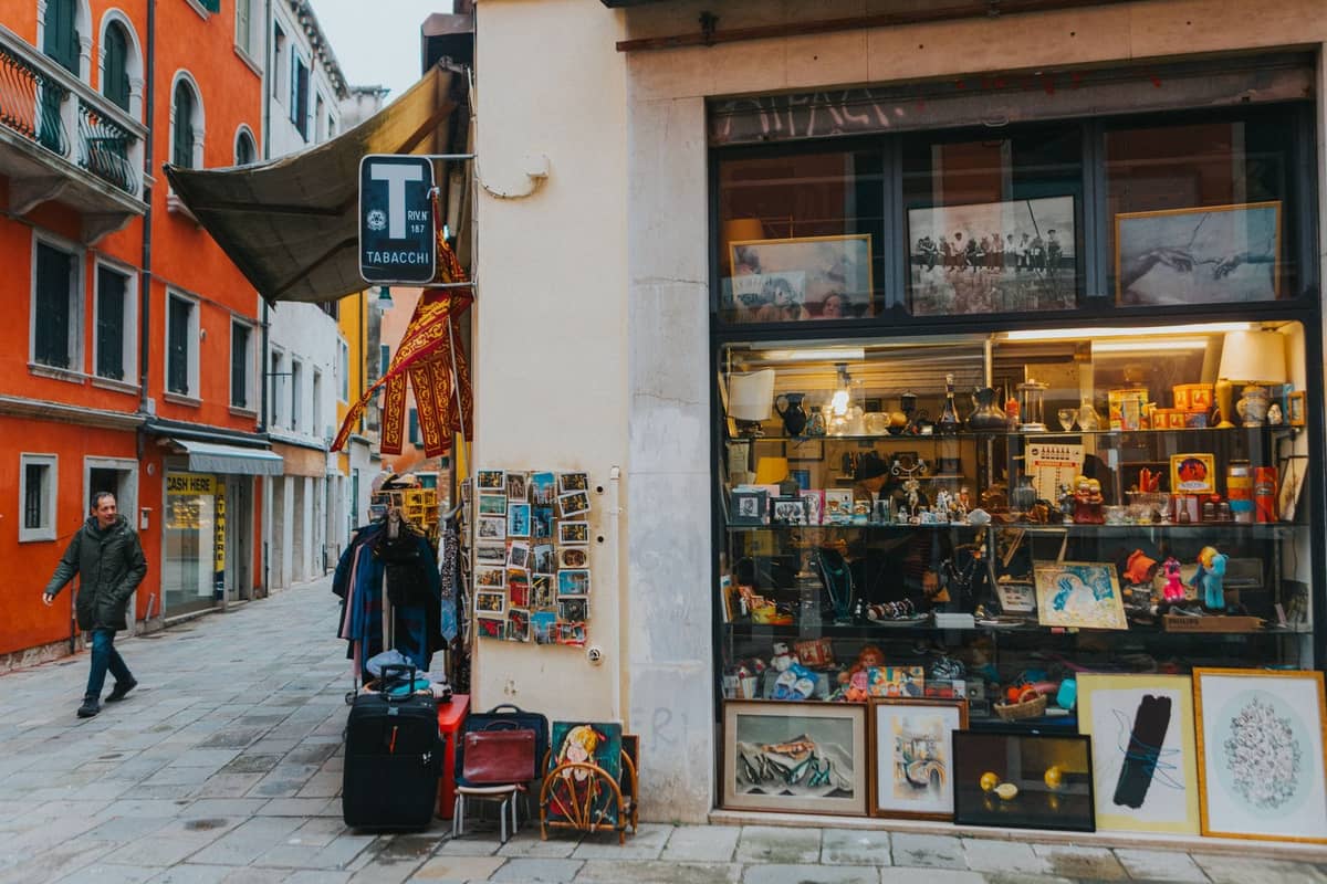 Venezianische Straßenecke mit einem lokalen Geschäft, das Souvenirs, Kunst und Geschenke verkauft, umgeben von bunten Gebäuden und ruhigen Steinstraßen.