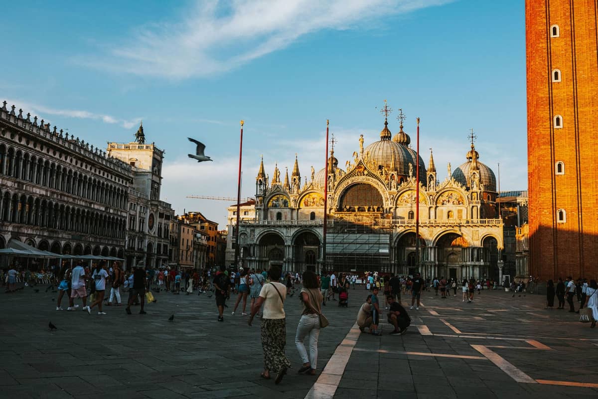 Der Markusplatz in Venedig mit Spaziergängern und der Basilica di San Marco im Hintergrund unter blauem Himmel.