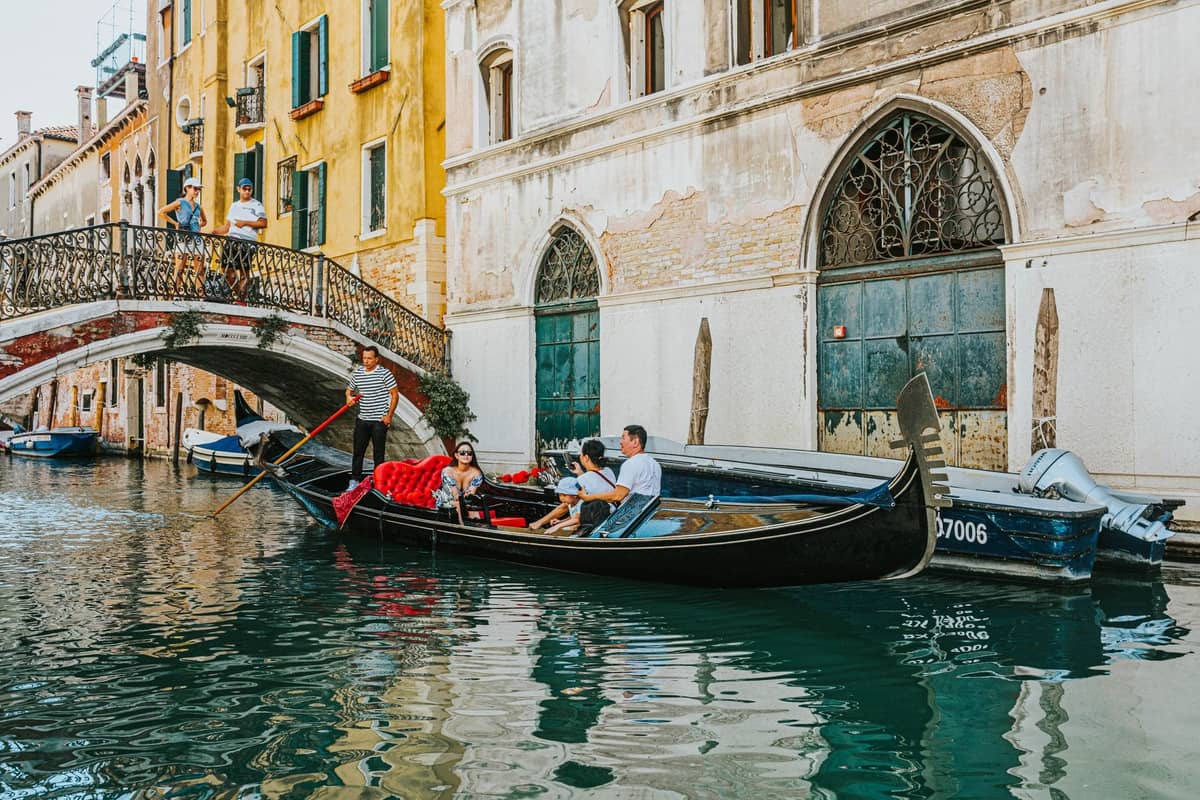 Eine Familie genießt eine Gondelfahrt unter einer kleinen Brücke entlang eines der malerischen Kanäle Venedigs, umgeben von klassischer venezianischer Architektur.