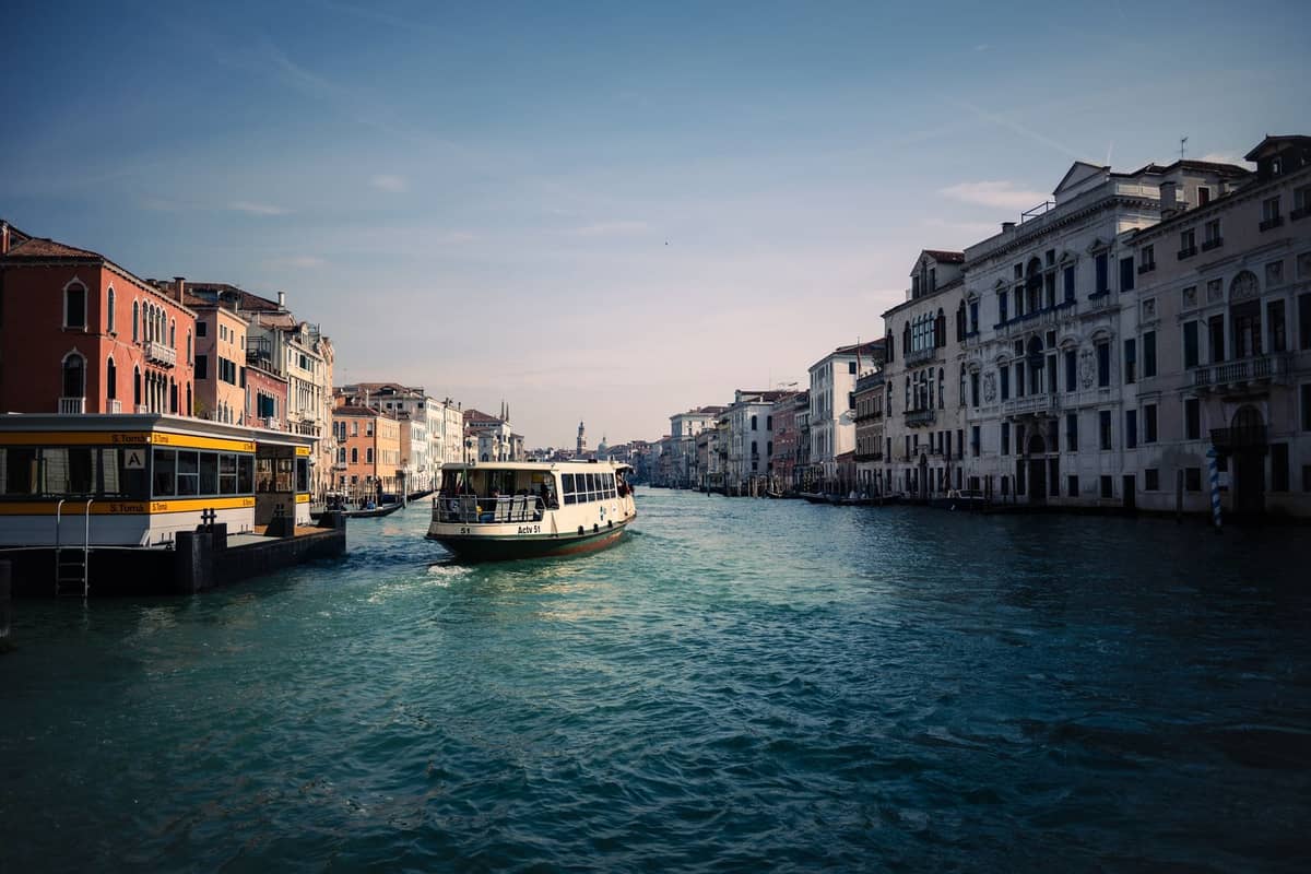 Ein öffentliches Vaporetto-Wasserbus fährt den Canal Grande in Venedig entlang, umgeben von historischen venezianischen Gebäuden auf beiden Seiten unter einem klaren Himmel.