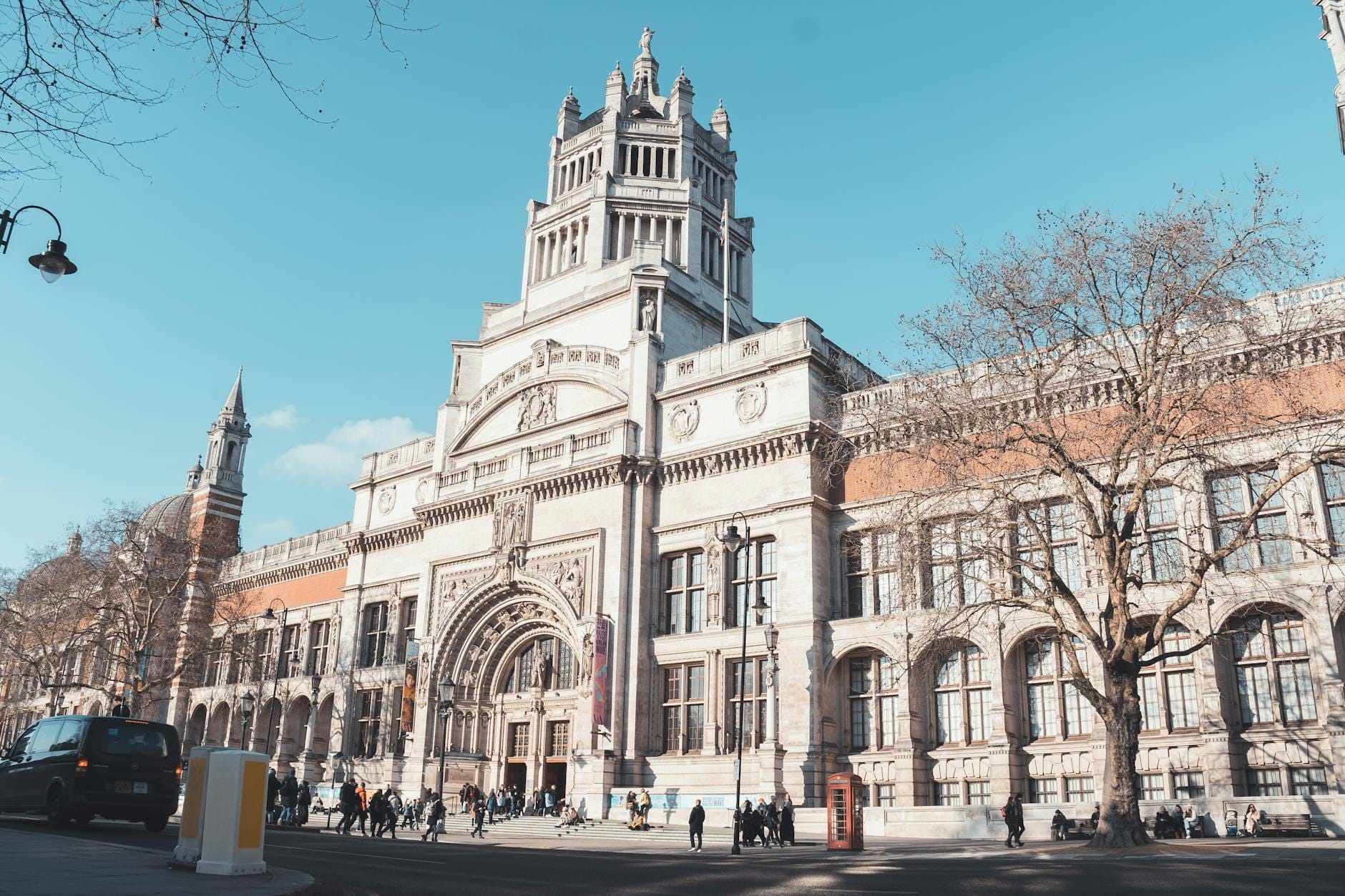 Vista panoramica della maestosa facciata del Victoria and Albert Museum con persone che passeggiano fuori sotto un cielo azzurro limpido a South Kensington, Londra.