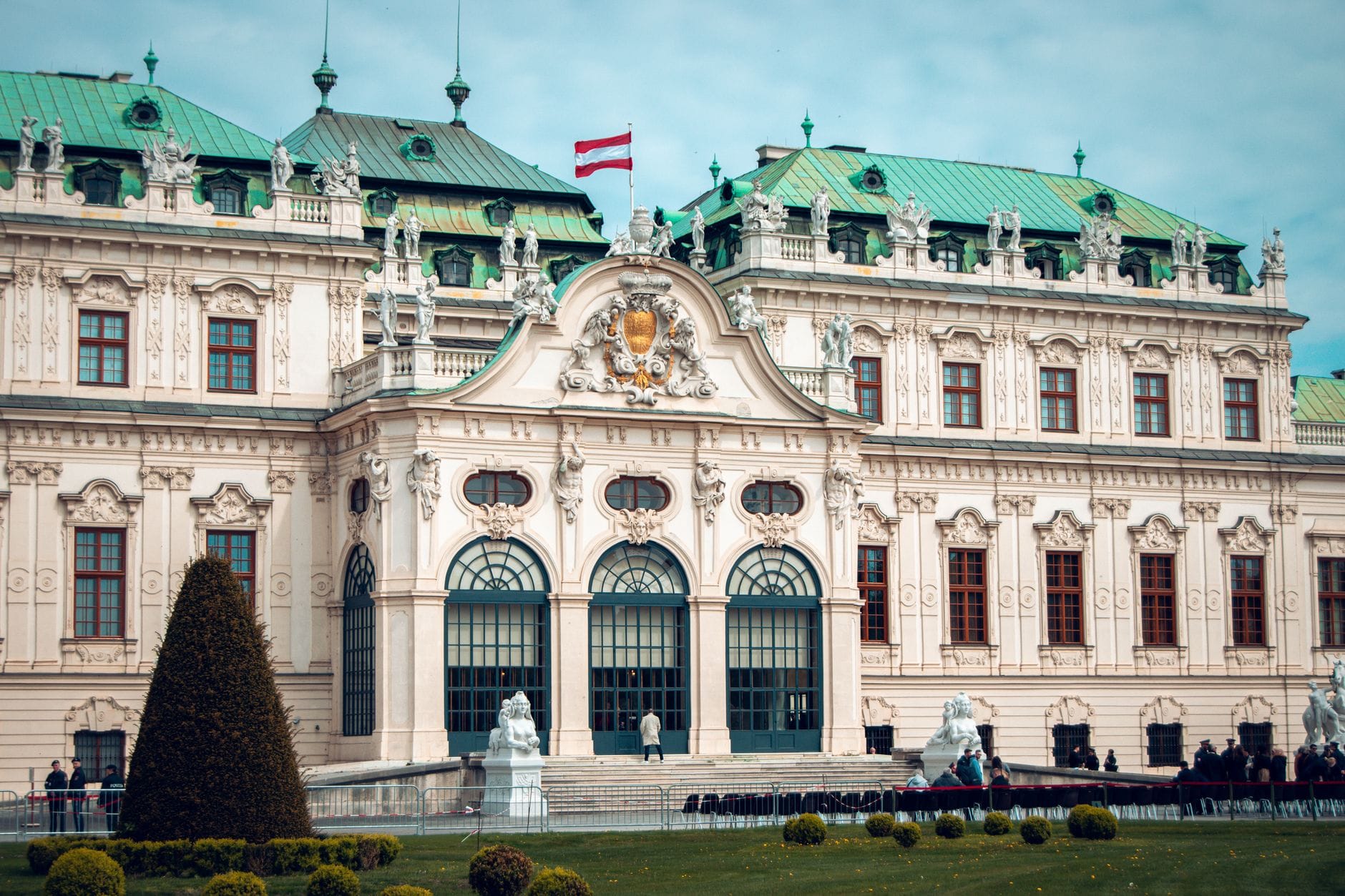 Fachada barroca ornamentada del Palacio del Upper Belvedere en Viena, con la bandera austriaca en el tejado y estatuas de jardín en el frente.