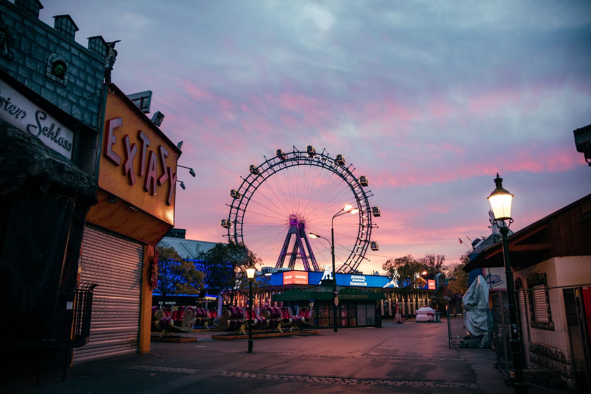 El parque de atracciones Prater de Viena al atardecer con la iluminada Riesenrad bajo un cielo vespertino rosa y azul.