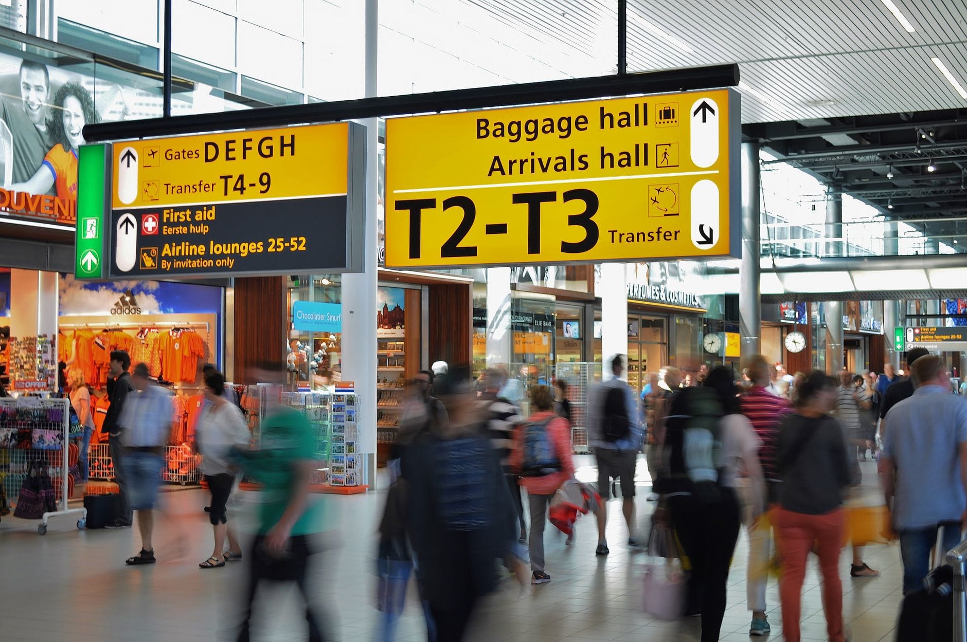 Belebte Flughafenhalle mit Reisenden, Gepäck und auffälligen gelben Ankunfts- und Transitschildern.