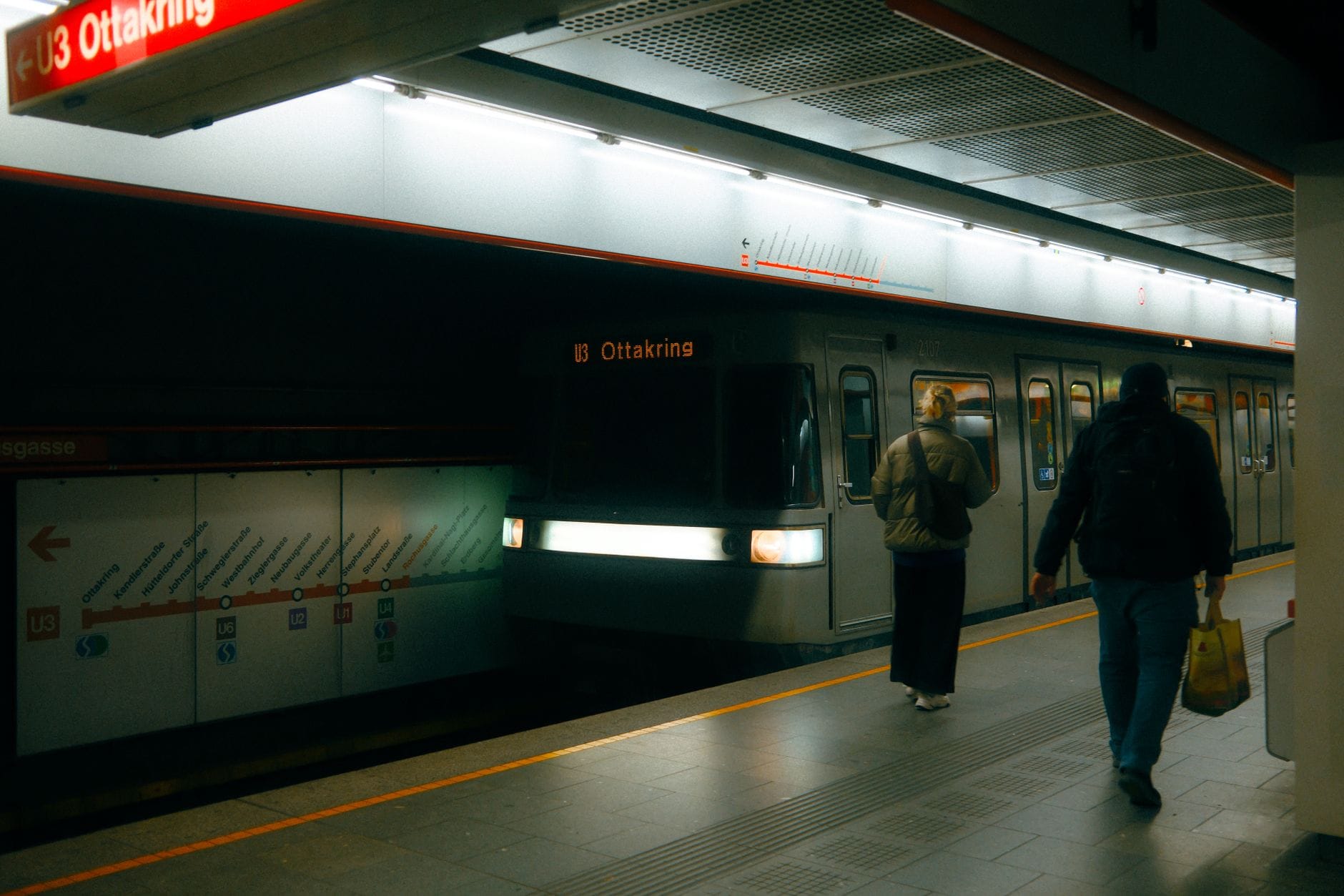Wien U-Bahn-Station mit einem Zug in Richtung Ottakring, Fahrgästen auf dem Bahnsteig und einer U-Bahn-Karte an der Wand.