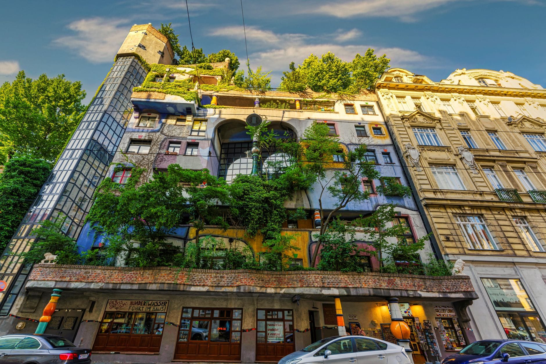 Bunte, verspielte Fassade des Wiener Hundertwasserhauses mit üppigem Grün und einzigartigem architektonischen Design, von der Straßenebene aus gesehen.