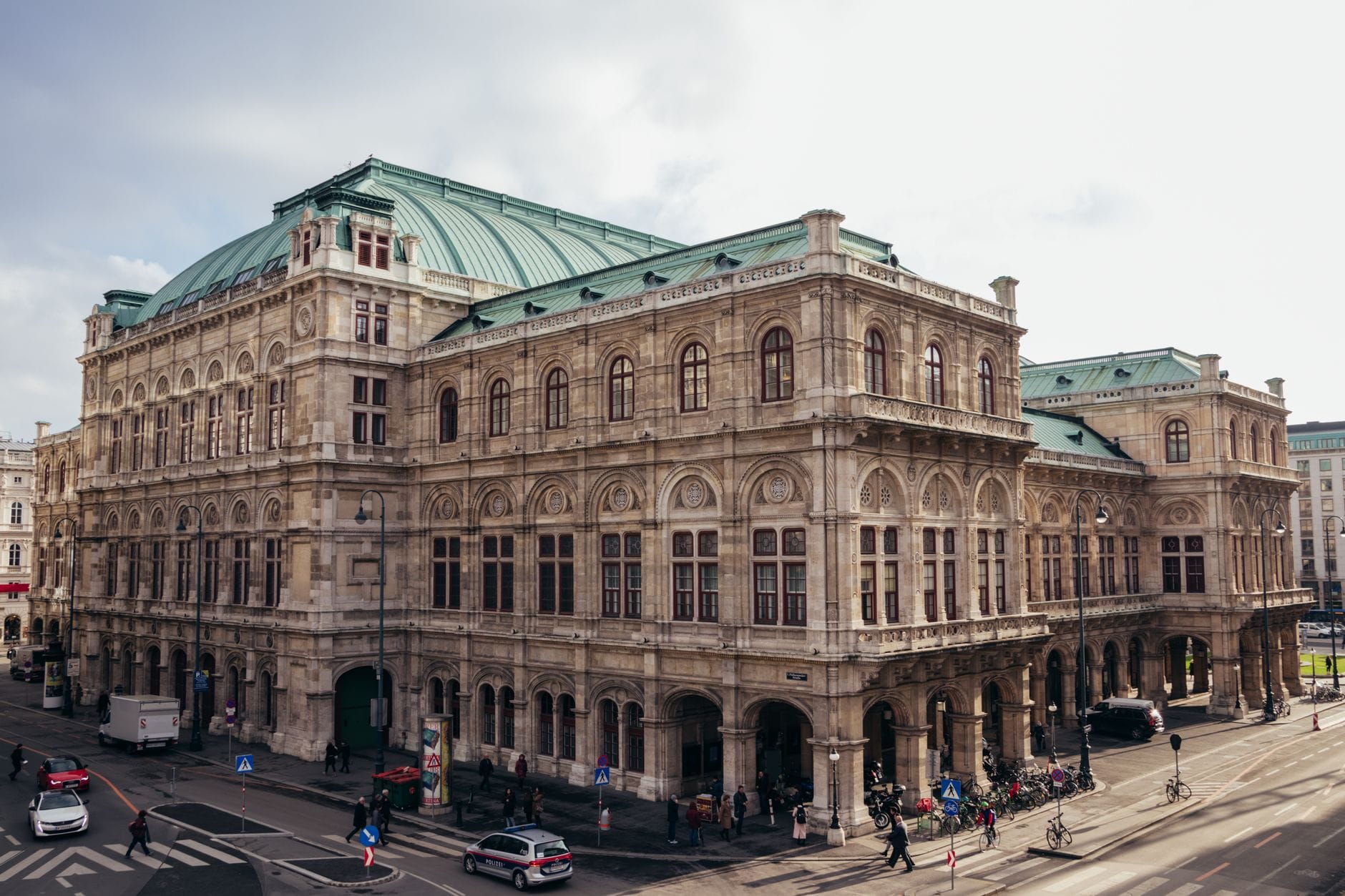 Ein prächtiges Gebäude aus dem 19. Jahrhundert mit aufwendiger Steinmetzarbeit und einem grünen Kupferdach an einer belebten Kreuzung, typisch für die Architektur der Wiener Ringstraße.