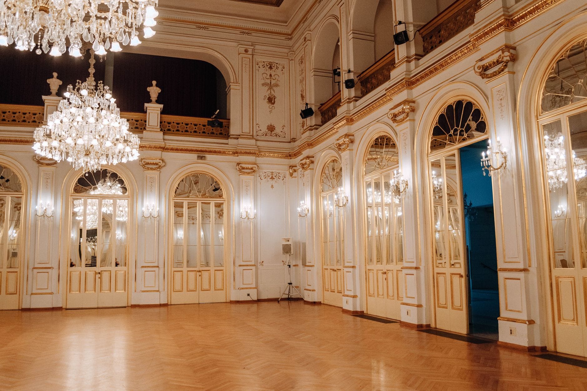 Eleganter, prächtiger Wiener Ballsaal mit Kronleuchtern, Parkettboden und verspiegelten Bogentüren, für ein formelles Event eingerichtet, aber derzeit leer.