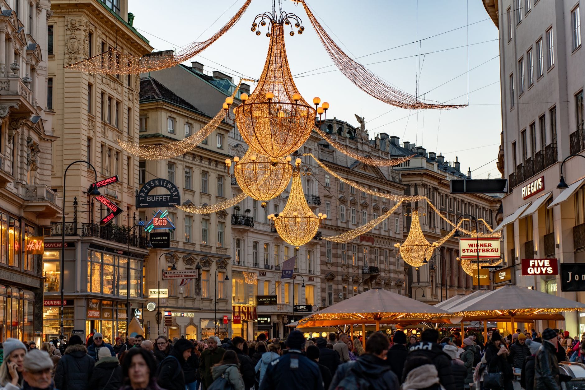Affollata strada di Vienna con candelieri natalizi festivi in alto, edifici storici, bancarelle di mercato all'aperto e atmosfera serale di festa.
