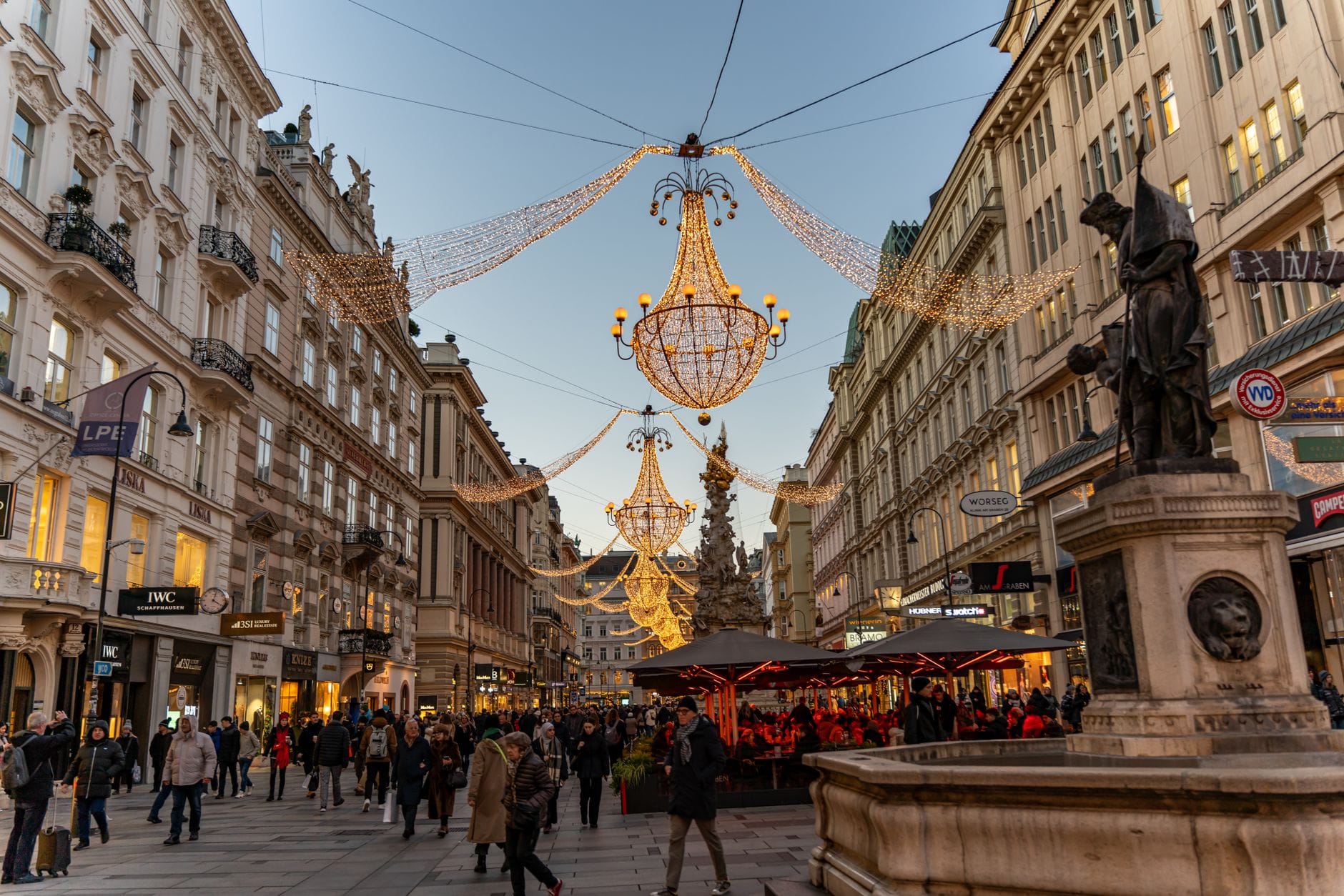 Scena festiva a Vienna con luci di Natale, un mercato, edifici storici e persone che camminano in una strada pedonale decorata.