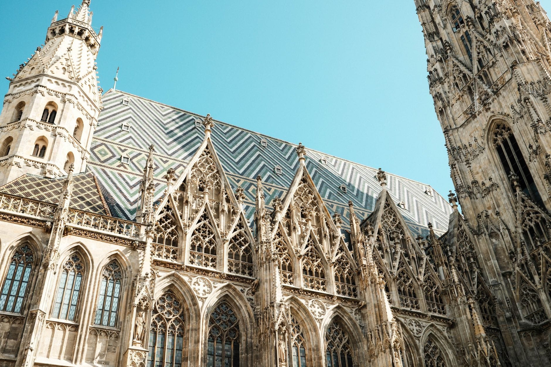 Detailansicht des Stephansdoms in Wien mit seinem aufwendigen gotischen Steinmetzwerk und dem bunten gemusterten Dach vor einem klaren blauen Himmel.