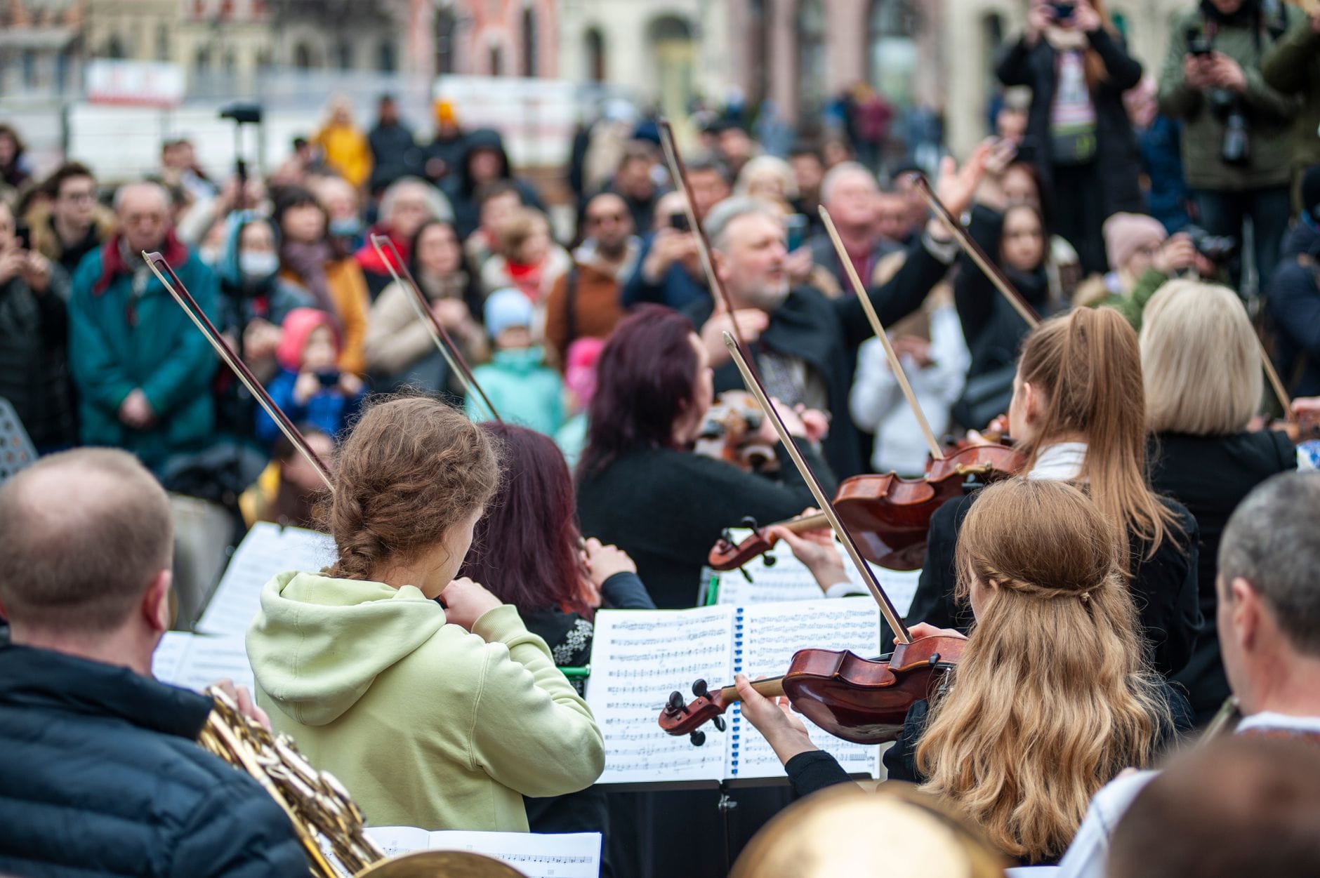 Klassisches Freiluftkonzert mit Musikern, die Streichinstrumente für eine große Menschenmenge in einer europäischen Stadtkulisse spielen.