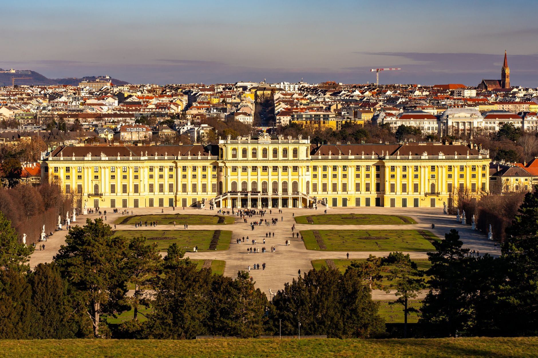 Schloss Schönbrunn in Wien mit seinen Gärten, Stadtpanorama im Hintergrund, an einem klaren sonnigen Tag mit Besuchern im Vordergrund fotografiert.