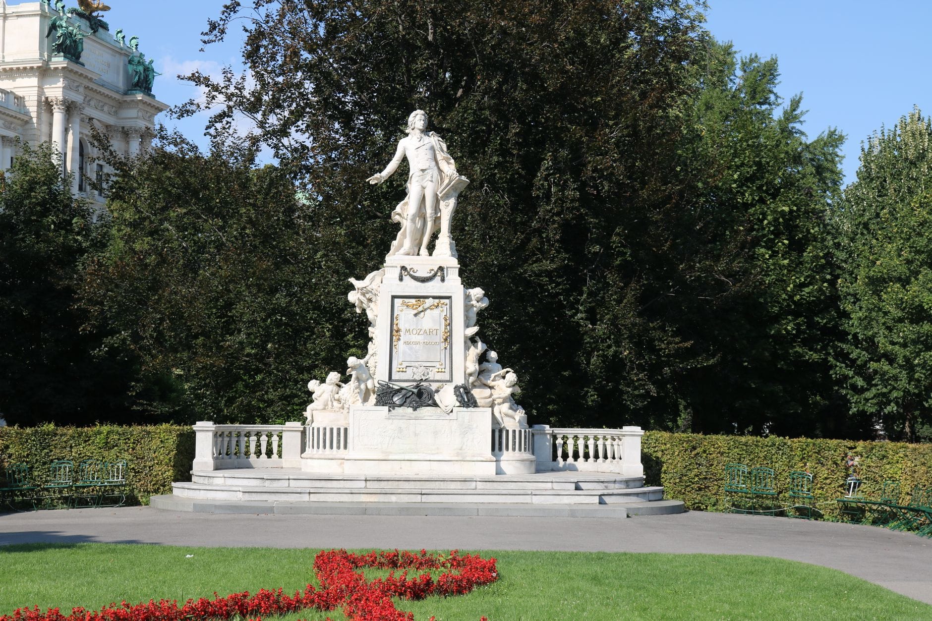 Mozart-Statue in einem Park in Wien mit gepflegten Blumenbeeten und Bäumen im Hintergrund.