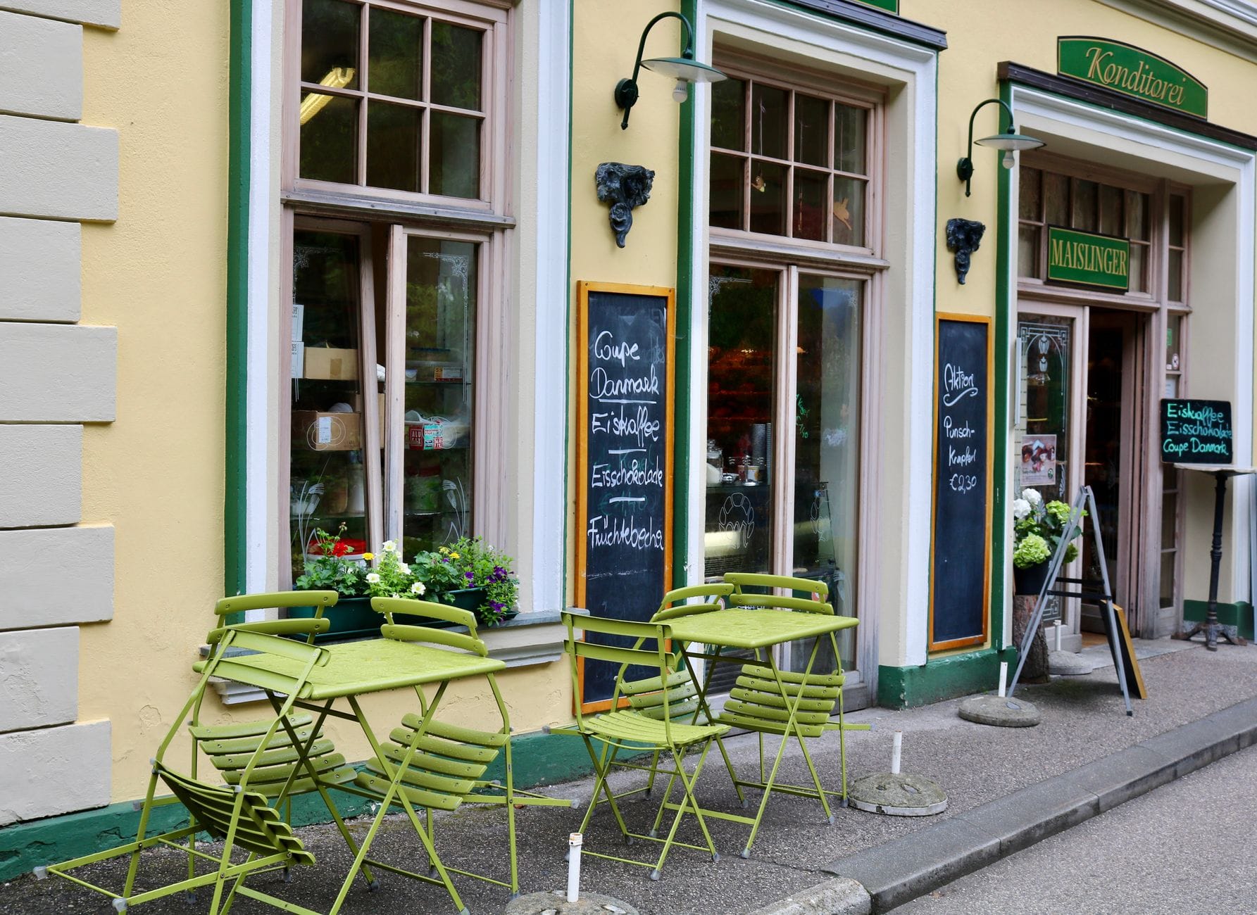 Charmante Außenansicht eines traditionellen Wiener Kaffeehauses mit grünen Tischen und Stühlen auf dem Gehsteig, großen Fenstern und handgeschriebenen Menütafeln.