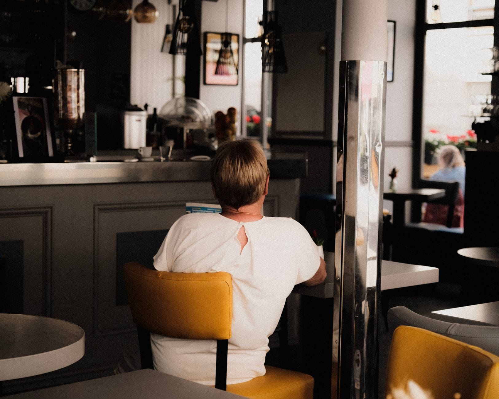 Persona seduta da sola a un tavolo in una caffetteria accogliente e alla moda con sedie gialle e un'atmosfera rilassata.