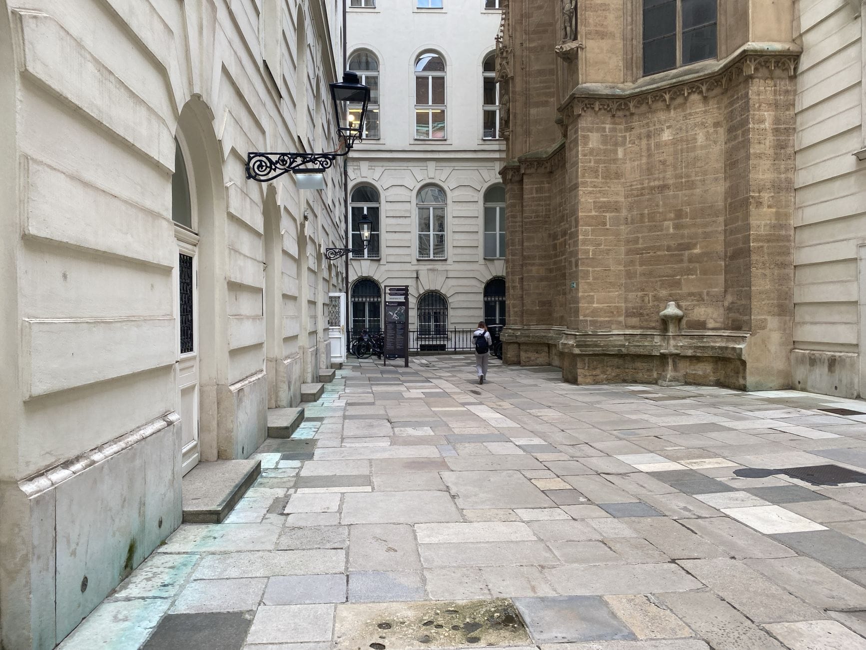 Schmale Kopfsteinpflastergasse in Wiens historischem Zentrum, eingerahmt von klassischer Architektur und einer Vintage-Laterne, mit einer einzelnen Person in der Ferne.