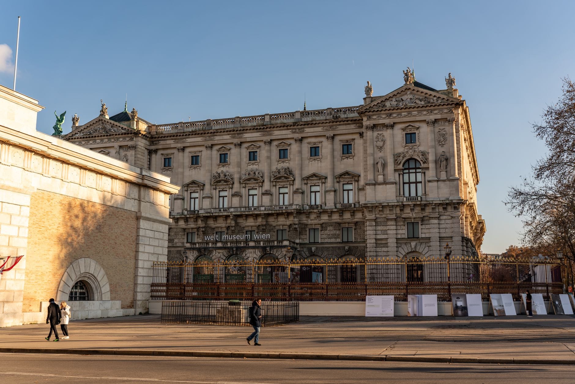 Weltmuseum Wien — величественное историческое здание с богатой архитектурой, снятое с противоположной стороны улицы, по которой прогуливаются пешеходы в Вене