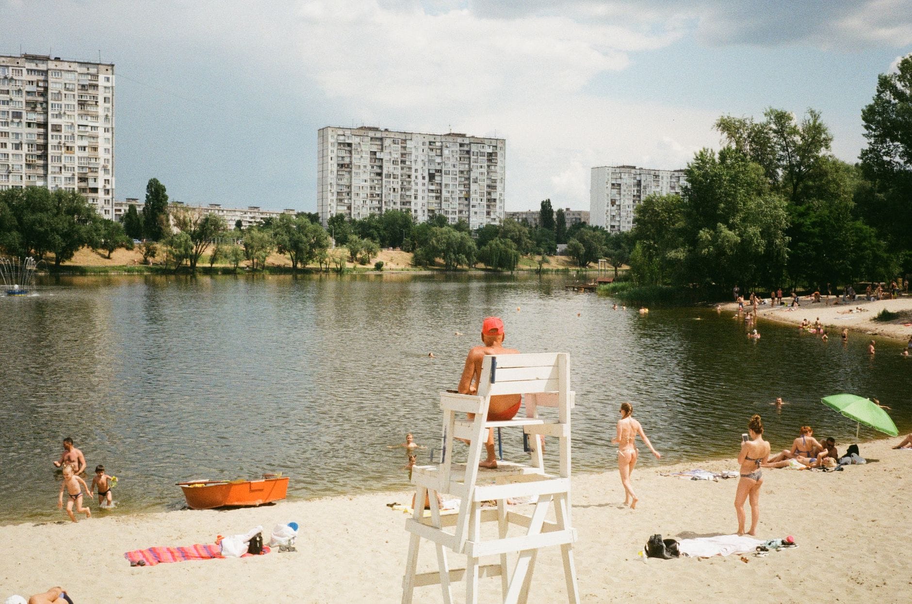 Städtischer Seebadestrand in Wien mit schwimmenden und sonnenbadenden Menschen, Hochhäusern und grünen Bäumen im Hintergrund.