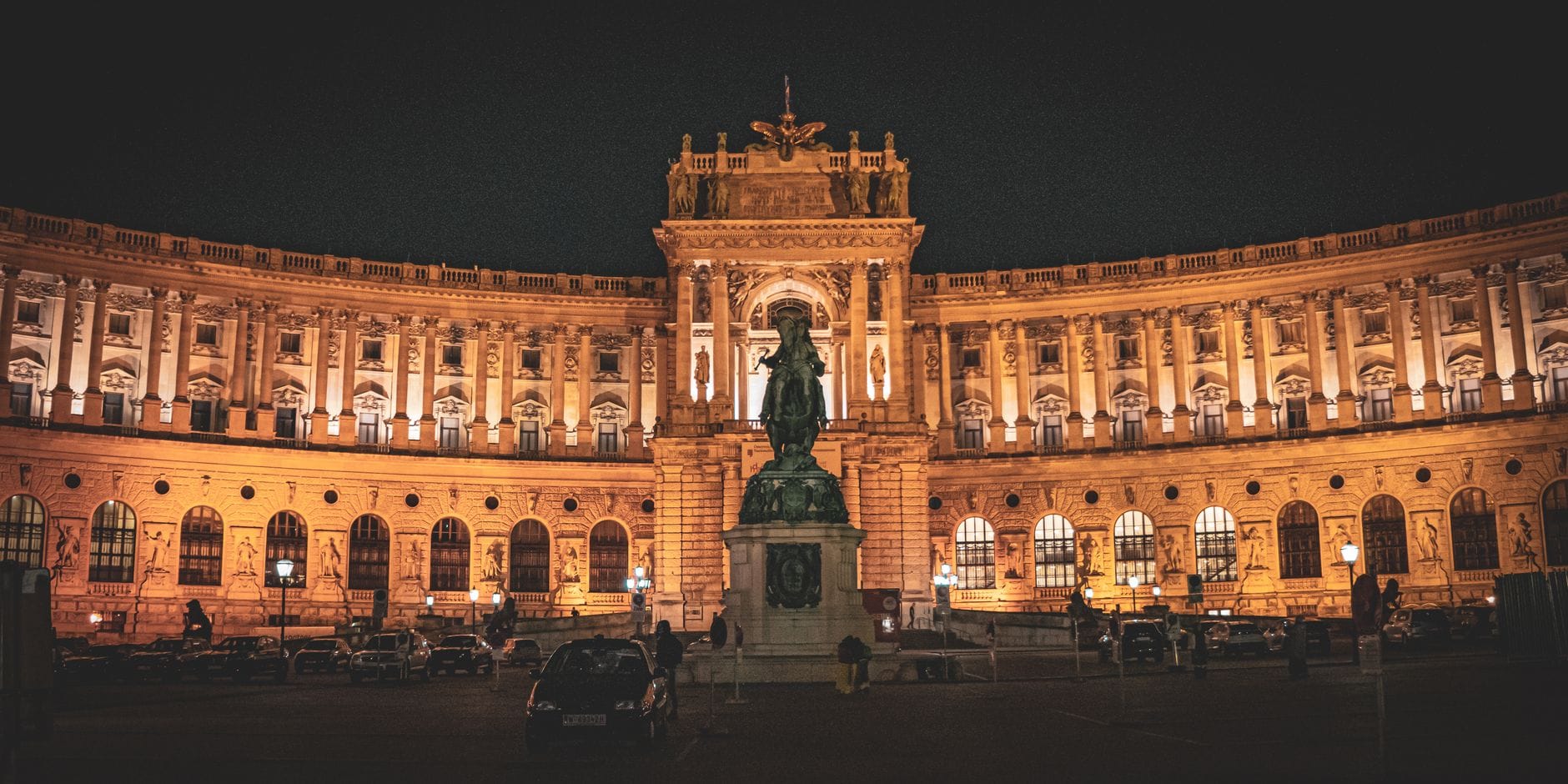 Facciata illuminata del Palazzo Hofburg di notte con una statua davanti, che mostra la grandiosa architettura di Vienna, perfetta per la stagione dei balli.