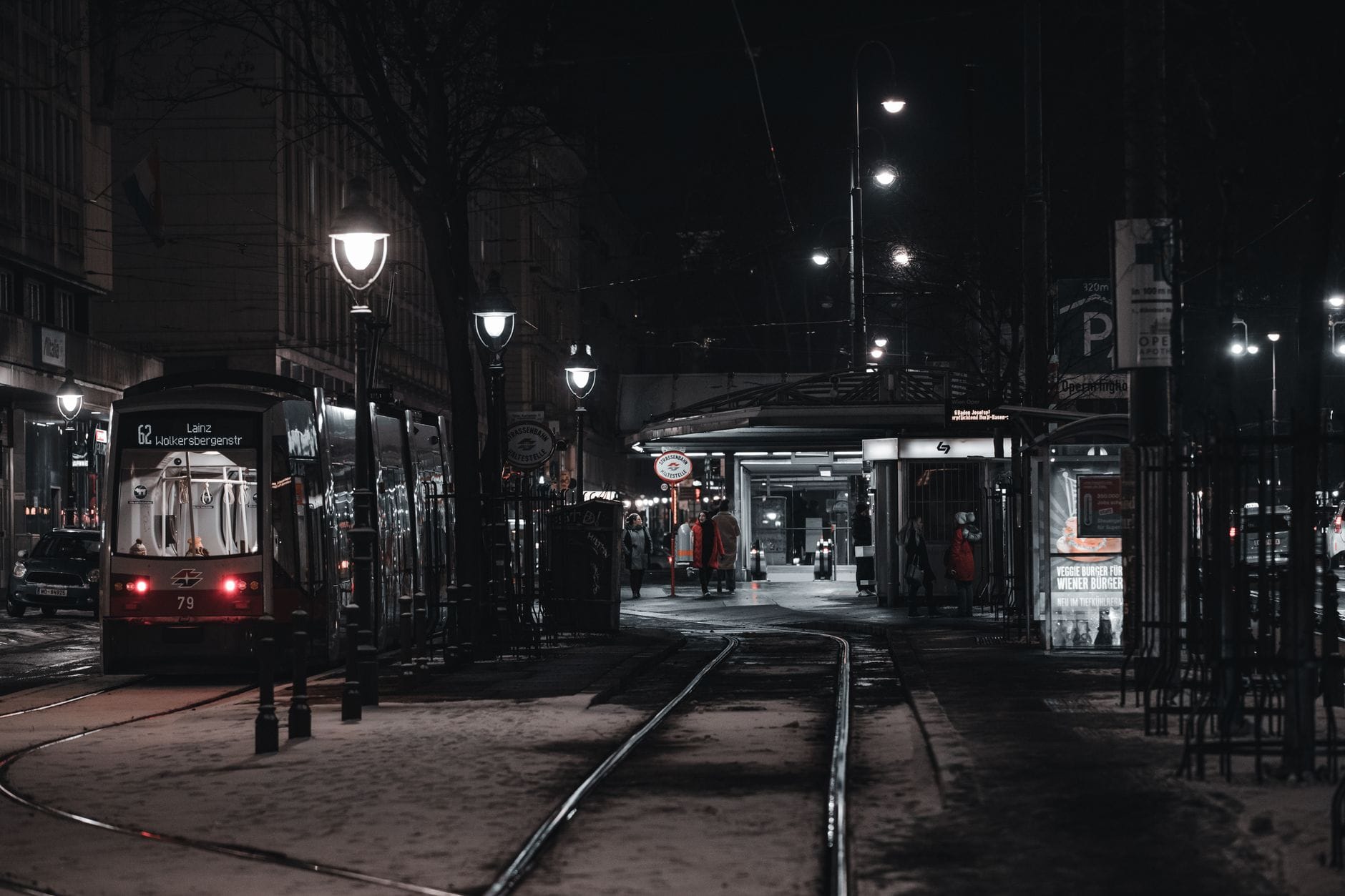 Strada di Vienna di notte in inverno con un tram in arrivo a una fermata, binari e leggera neve visibili.