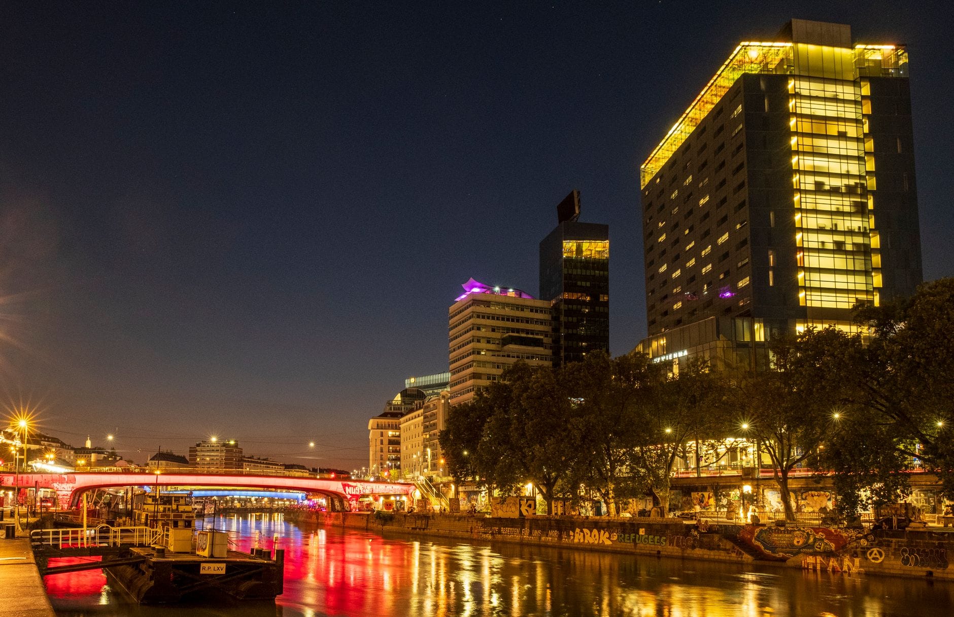Nächtlicher Blick auf Wien entlang des Donaukanals mit bunten Lichtern, die Bars, Clubs und Gebäude am Ufer erleuchten – mitten im pulsierenden Nachtleben der Stadt.