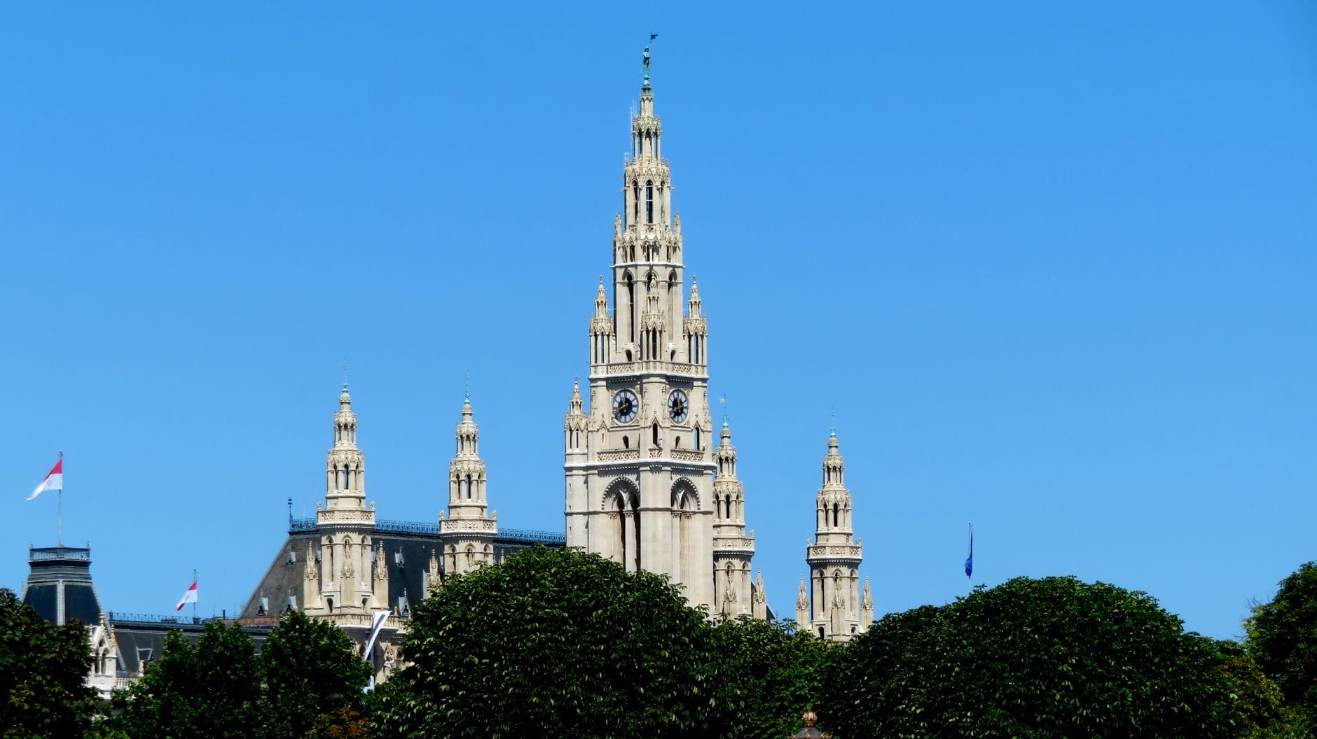 Vista diurna del Ayuntamiento Rathaus de Viena con cielo azul y árboles verdes en primer plano, mostrando el monumento sin aglomeraciones estacionales.