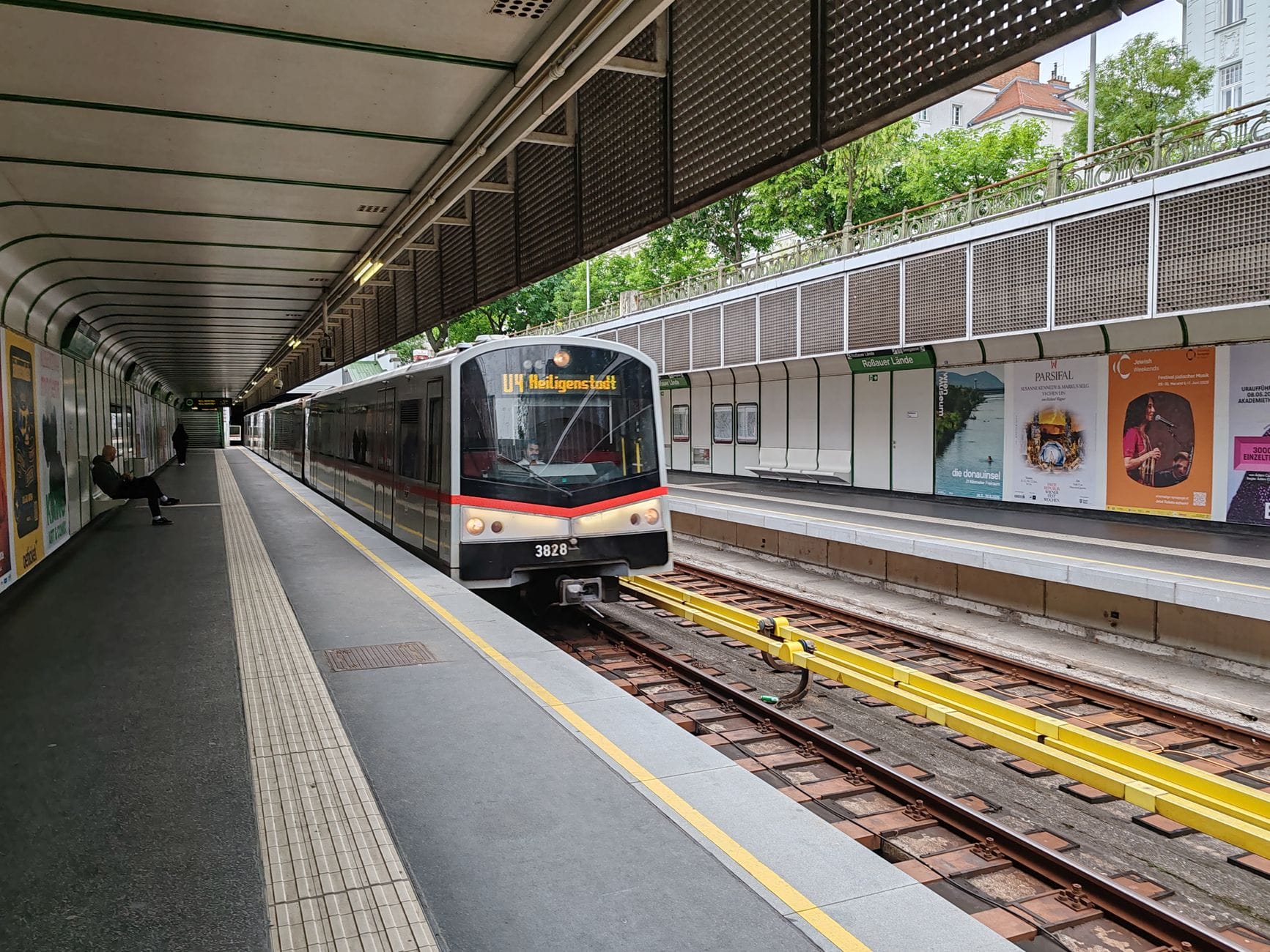 Tren del U-Bahn de Viena llegando a una plataforma exterior limpia con señalización clara y pasajeros esperando.