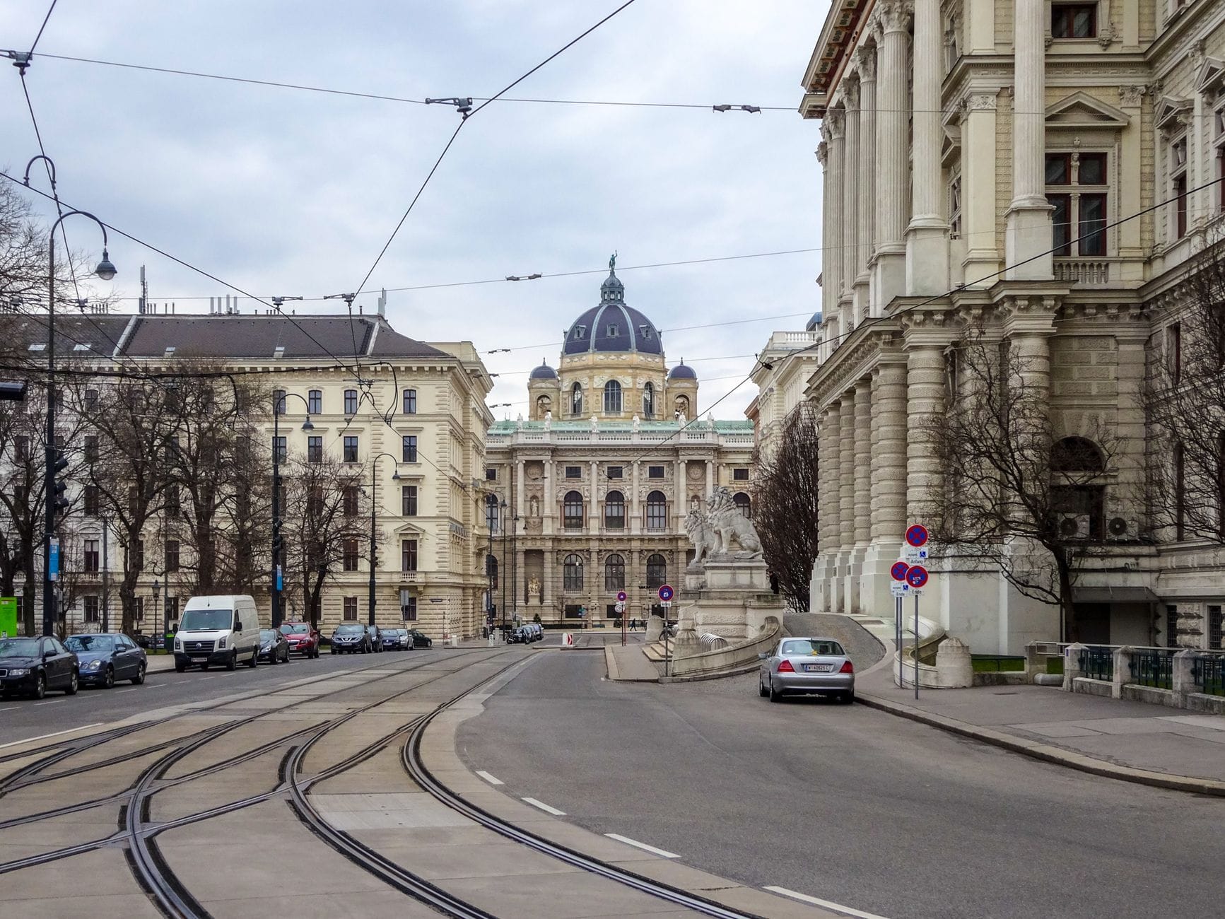 Vista de la Ringstrasse de Viena con grandiosos edificios históricos, vías de tranvía, coches y la cúpula del Museo de Historia Natural al fondo.